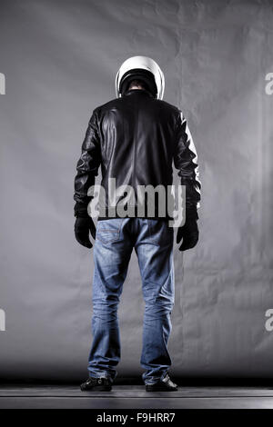 Autofahrer mit einem Helm, Lederjacke und Jeans auf Grunge Hintergrund mit grellem Licht Stockfoto