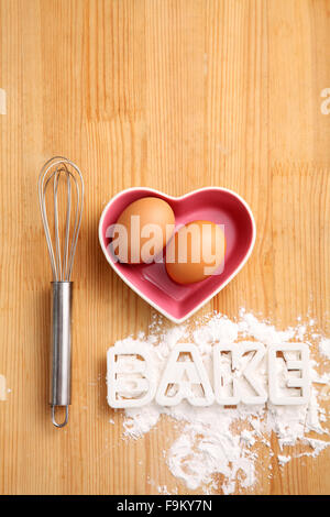 Backen, Konzept, Hand Schneebesen und Eiern in einem Herz-Form-container Stockfoto