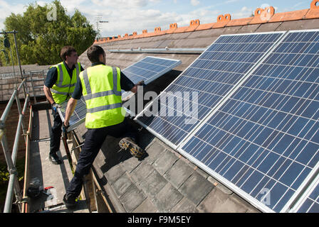 Arbeiter installieren Photovoltaik-Solarzellen auf das Schieferdach ein viktorianisches Haus in London, England. Stockfoto