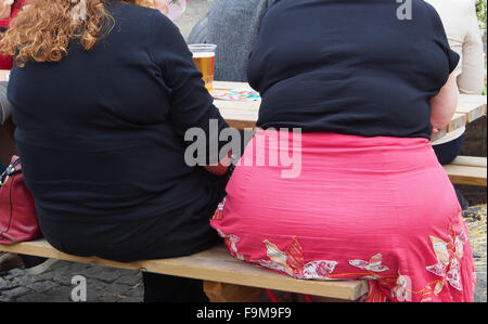 Rückansicht des zwei übergewichtige Frauen sitzen auf einer Bank außerhalb der Manchester Food and Drink Festival 2015 trinken. Stockfoto