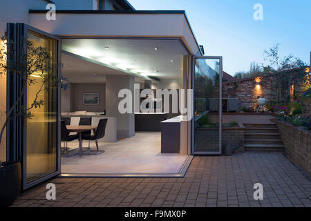 Küche und Esszimmer Bereiche gesehen durch Bi-Fold Türen von Terrasse und Garten in der Dämmerung geöffnet. Ein modernes Einfamilienhaus. Stockfoto