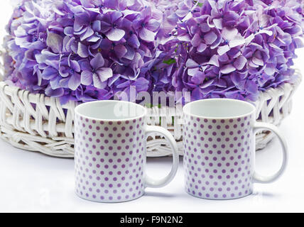 Hortensien in einem Korb auf weißem Hintergrund und zwei Kaffeetassen Stockfoto