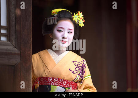 Eine Frau gekleidet wie eine traditionelle Maiko aus einem Eingang Tempel in Kyoto, Japan aussieht. Stockfoto