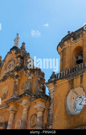 Nahaufnahme der gelben Kirche mit White Uhr, Jesus-Stein-Skulptur und eine Glocke unter blauen Himmel ohne Wolken Stockfoto