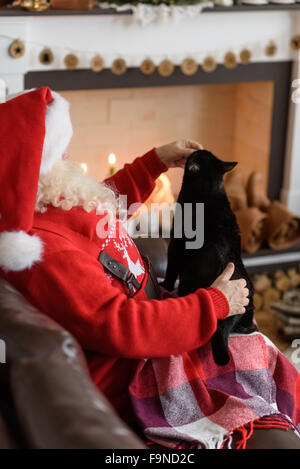 Santa Claus Erwärmung Fütterung seiner Katze zu Hause Stockfoto