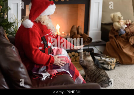 Santa Claus Erwärmung Fütterung seiner Katze zu Hause Stockfoto