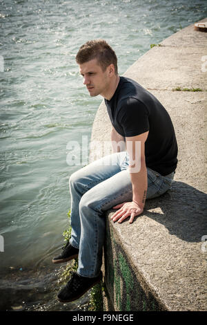 3/4 Länge des kontemplativen Licht braun behaarte Teenager tragen grüne Kapuzen-Shirt und Jeans Jeans sitzen auf Wand Stockfoto