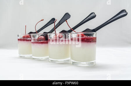 Joghurt Penna Cotta mit roten Kirschen und Beeren Marmelade in Gläser und Löffel auf weichen Ton Hintergrund Stockfoto