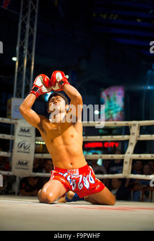 Knienden männlichen Muay thai Kickboxer in roten Badehose seine Arme, nachschlagen und singen während eines Rituals traditionellen Kickboxen Stockfoto