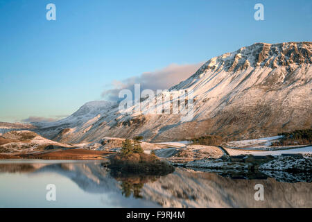 Die Winter tief verschneiten Hänge des Gebirges Cader Idris spiegeln sich im ruhigen Wasser der Cregennen Seen. Stockfoto