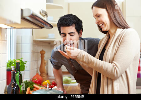 Lächelnde Frau Mann eine Suppe mit einem Holzlöffel in der Küche schmecken zu lassen Stockfoto