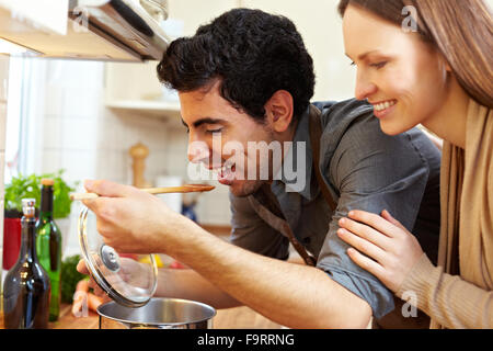 Mann, die Suppe auf dem Herd in der Küche zu probieren, während glückliche Frau zusieht Stockfoto