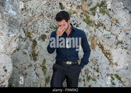 Eine halbe Stelle erschossen eines wunderschönen jungen Geschäftsmann gegen Boulder mit Händen in den Taschen und in die Kamera schaut. Stockfoto