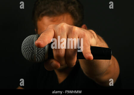 Mann mit Hand-Mikrofon mit Teufelshörnern rock Blechschild und Gesicht hinter auf schwarzem Hintergrund Stockfoto