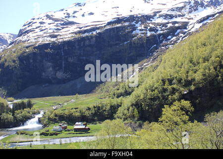 Blick von der Flamsbana (Flam Railway) eines kleinen Dorfes mit einem Fluss und Berg Stockfoto