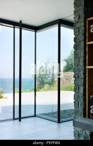 Die Innenräume von einem modernen Haus auf den Klippen mit Blick aufs Meer. Große Glasflächen und Stadtmauern und Holzregale und Raumteiler. Stockfoto