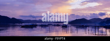 Pretty Pink orange Sky Wolkengebilde über eine Insel mit Reflexion und traditionellen philippinischen Holzboote bei Sonnenuntergang auf der Insel Coron Stockfoto