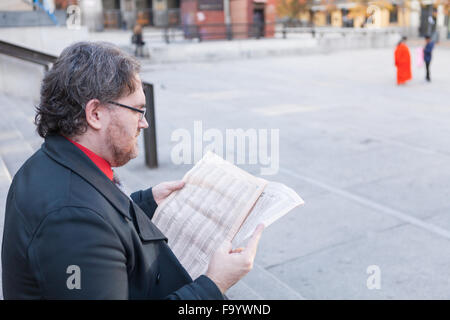 Ein junger Geschäftsmann mit Brille lesen einer Zeitung ist das Denken in städtischen Szene Stockfoto