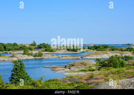 Kleine Hütten auf einer Schäre in den Schären. Eingebettet von grünen Bäumen. Wasser und niedrigen Schären vorne und hinten. Blauer Himmel. Stockfoto