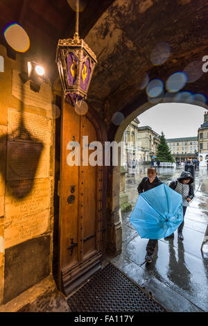 Shopper hetzen, um Schutz vor dem schweren Regen im Eingangsbereich der Abteikirche von Bath am "Panic Samstag" am letzten Wochenende vor Weihnachten statt. Stockfoto