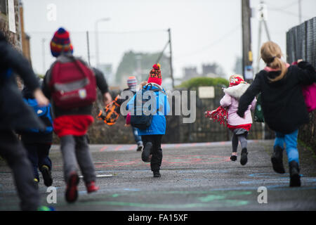 Eine Gruppe von primären Schulkinder schneidigen Rauschen läuft aus ihrer kleinen Landschule am Ende des Tages zu Beginn des Urlaubs am Wochenende oder an Feiertagen. Wales UK Stockfoto