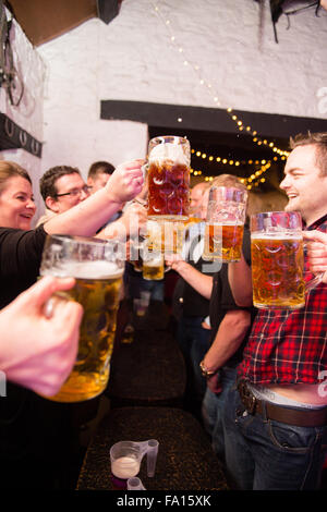 Eine Gruppe von Männern und Frauen Spaß amüsieren sich Bier trinken und Lager aus Glas "Bierkrüge" bei einer deutschen Themen Bavarian Stompers Party-Nacht in einer Kneipe, Wales UK Stockfoto