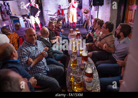 Eine Gruppe von Männern und Frauen, Arme, verbindet singen und schwingen, Spaß, Vergnügen sich Bier trinken und Lager aus Glas "Bierkrüge" bei einer deutschen Themen Bavarian Stompers Party-Nacht in einer Kneipe, Wales UK Stockfoto