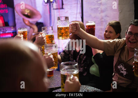 Eine Gruppe von Männern und Frauen Spaß amüsieren sich Bier trinken und Lager aus Glas "Bierkrüge" bei einer deutschen Themen Bavarian Stompers Party-Nacht in einer Kneipe, Wales UK Stockfoto