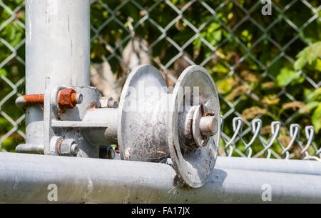 Dreckig abgenutzt Metallwalze im Rahmen der Chain-link fence Tor mit verrosteten Schraube und Mutter. Stockfoto