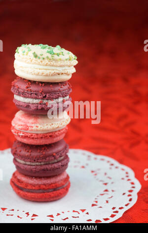 Stapel von Weihnachten Macarons, Vanille & Basilikum, mattierte Preiselbeere, Zuckerstange und Glühwein Wein Aromen auf roten Tischdecke Stockfoto