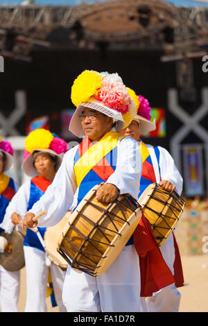 Ein älterer senior Mann eine traditionellen koreanischen Trommel spielen statt zusammen mit Seil in bunten Kleidern bei einem lokalen Outdoor-festival Stockfoto