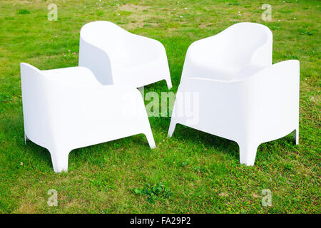 Vier moderne weiße Plastikstühle stehen auf frischen grünen Rasen Stockfoto
