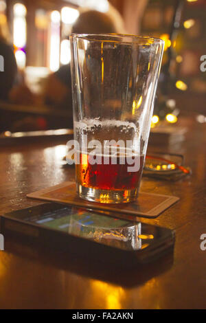 Nahaufnahme von einem meist betrunken Bier, Brillen und ein Handy zeigt eine GPS-Karte sitzen auf eine Bar in einer dunklen Kneipe mit verschwommenen Gönner eine Stockfoto