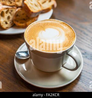 Kaffeetasse mit Sahne und Brot auf einem Holztisch Stockfoto