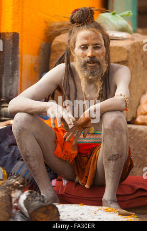 Eine Naga Baba Sadhu, Haut bedeckt in Asche, sitzen auf den Ghat entlang des Ganges Stockfoto