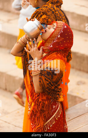 Eine junge indische Frau in roten Saree Gießen in Mund, Trinkwasser unhygienisch Ganges Fluss aus einer Urne nach hinduistischer Sitte Stockfoto