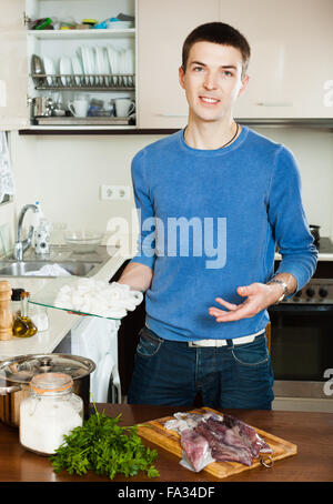 Gut aussehender Mann Kochen rohen Tintenfisch in Küche zu Hause Stockfoto