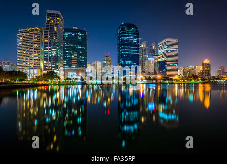 Moderne Wolkenkratzer und Lake Rajada in der Nacht, im Benjakiti Park in Bangkok, Thailand. Stockfoto