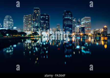 Moderne Wolkenkratzer und Lake Rajada in der Nacht, im Benjakiti Park in Bangkok, Thailand. Stockfoto