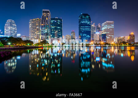 Moderne Wolkenkratzer und Lake Rajada in der Nacht, im Benjakiti Park in Bangkok, Thailand. Stockfoto