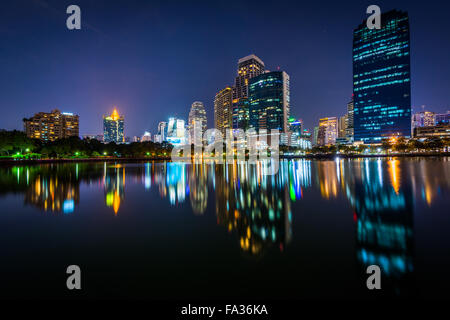 Moderne Wolkenkratzer und Lake Rajada in der Nacht, im Benjakiti Park in Bangkok, Thailand. Stockfoto