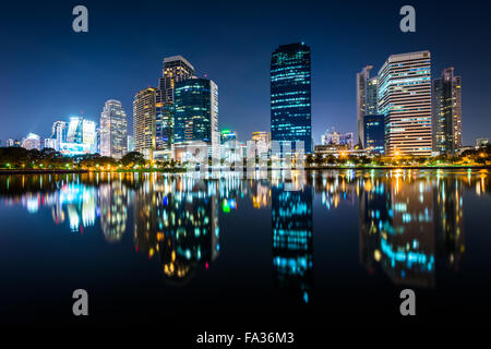 Moderne Wolkenkratzer und Lake Rajada in der Nacht, im Benjakiti Park in Bangkok, Thailand. Stockfoto