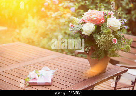 Geschenk mit Blumenstrauß auf Tisch im Garten, München, Bayern, Deutschland Stockfoto