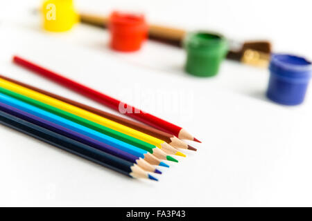 Nahaufnahme von bunte Bleistifte zum Zeichnen, liegen in der Nähe von Gouache Farben und Pinsel auf weißem Hintergrund Stockfoto