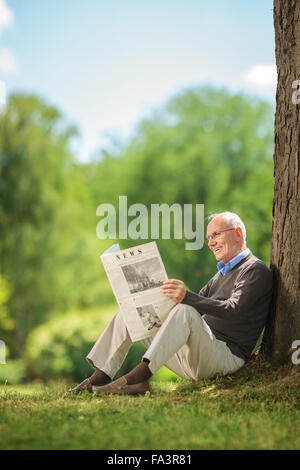 Vertikale Aufnahme eines freudigen senior Gentleman auf dem Rasen im Park sitzende Zeitung lesen Stockfoto