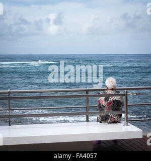 Ältere Frau sitzen auf der Bank mit Blick auf das Meer in Spanien. Stockfoto