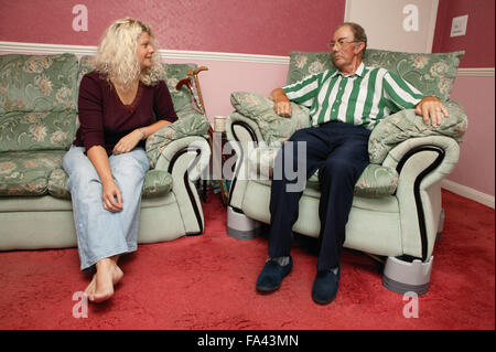 Menschen mit Parkinson-Krankheit im Stuhl mit Chairraising Blöcken ausgestattet; im Gespräch mit seiner Tochter, Stockfoto