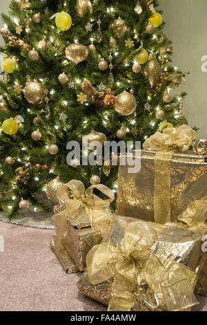 Schön verpackte Geschenke und gaben mit Bögen sind vor einer elegant geschmückter Weihnachtsbaum angeordnet. Stockfoto