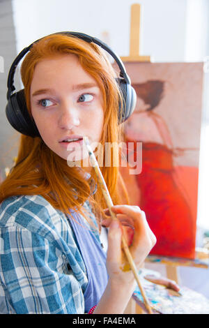 Nachdenklich attraktive junge Malerin anhören von Musik und Malerei in der Kunstwerkstatt Stockfoto