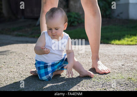 Baby Boy auf dem Bürgersteig sitzen und auf der Suche nach Kiesel, München, Bayern, Deutschland Stockfoto